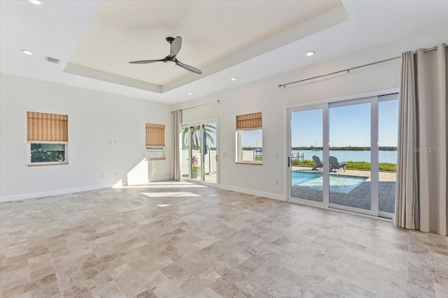 unfurnished living room with a raised ceiling, a healthy amount of sunlight, visible vents, and a water view