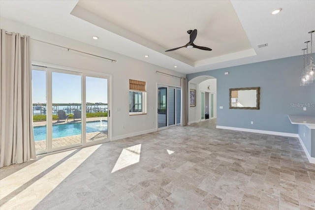 unfurnished living room with a raised ceiling, visible vents, arched walkways, and baseboards