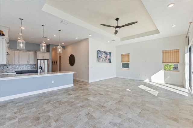 kitchen featuring open floor plan, decorative backsplash, stainless steel refrigerator with ice dispenser, a raised ceiling, and a sink