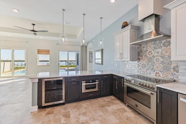 kitchen featuring a peninsula, wine cooler, appliances with stainless steel finishes, wall chimney range hood, and open floor plan