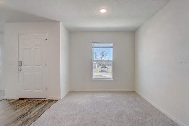 unfurnished room featuring baseboards, a textured ceiling, wood finished floors, and carpet flooring