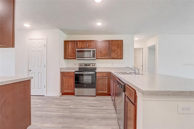 kitchen with a sink, stainless steel appliances, a peninsula, light wood finished floors, and light countertops