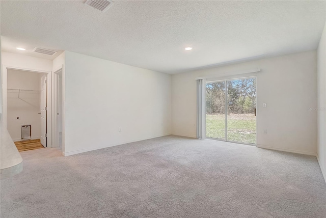 spare room with a textured ceiling, visible vents, and light carpet