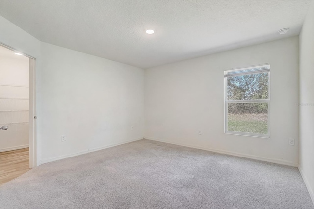 empty room with light carpet, a textured ceiling, and baseboards