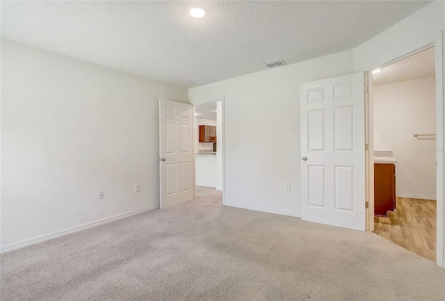 unfurnished bedroom with baseboards, light colored carpet, visible vents, and a textured ceiling