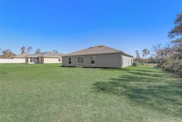 rear view of property featuring stucco siding, a yard, and fence