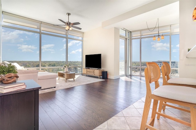 living room with ceiling fan with notable chandelier, a wall of windows, plenty of natural light, and wood finished floors