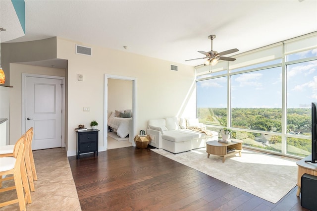 living area with a wall of windows, visible vents, wood finished floors, and a ceiling fan