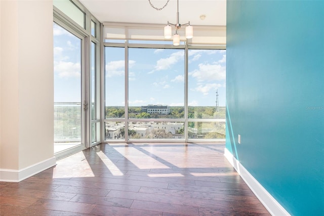 unfurnished room featuring a chandelier, wood finished floors, baseboards, and expansive windows