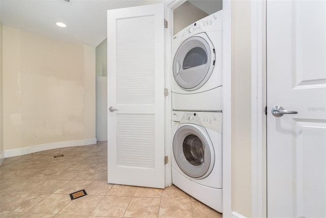 clothes washing area with laundry area, light tile patterned floors, baseboards, and stacked washer and clothes dryer