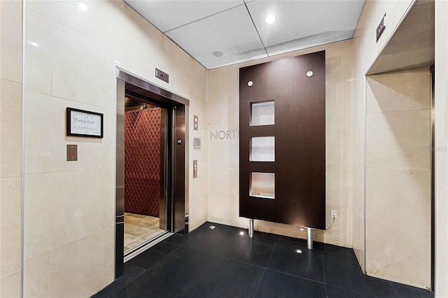 interior space with elevator, tile walls, and dark tile patterned floors