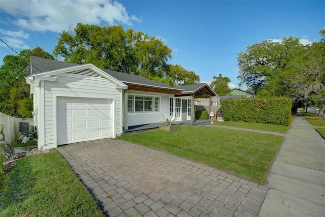 ranch-style house featuring a garage, decorative driveway, a front lawn, and fence