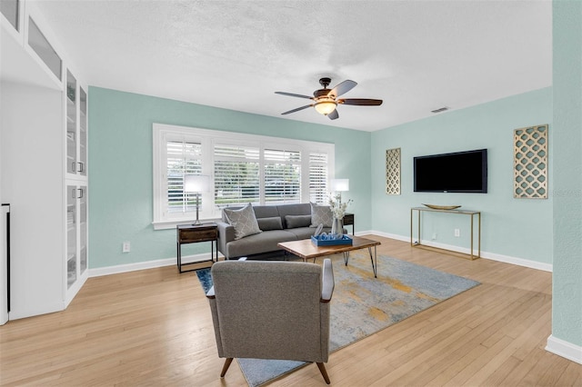 living area with visible vents, light wood-style flooring, baseboards, and a ceiling fan