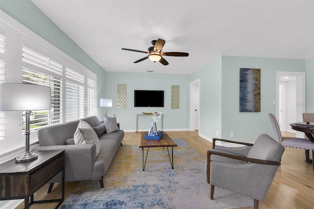 living area with baseboards, a ceiling fan, and wood finished floors