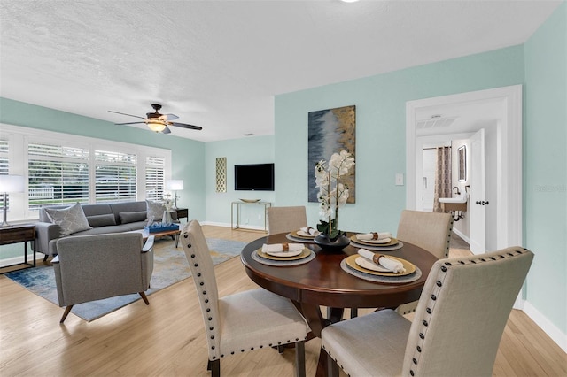 dining area with light wood-type flooring, baseboards, a textured ceiling, and ceiling fan