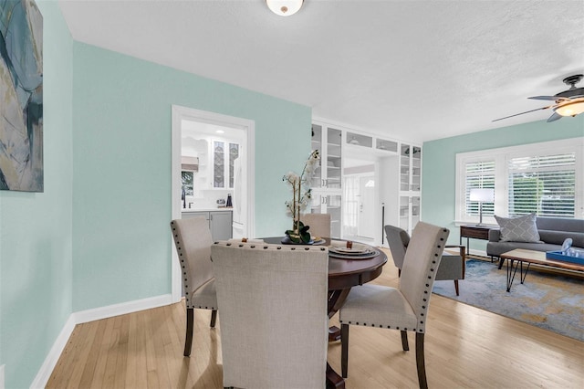 dining space featuring ceiling fan, baseboards, a textured ceiling, and light wood-style flooring