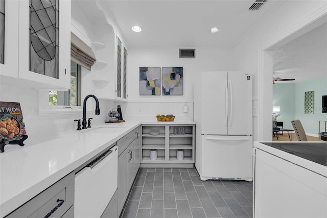 kitchen featuring visible vents, a sink, tasteful backsplash, white appliances, and glass insert cabinets