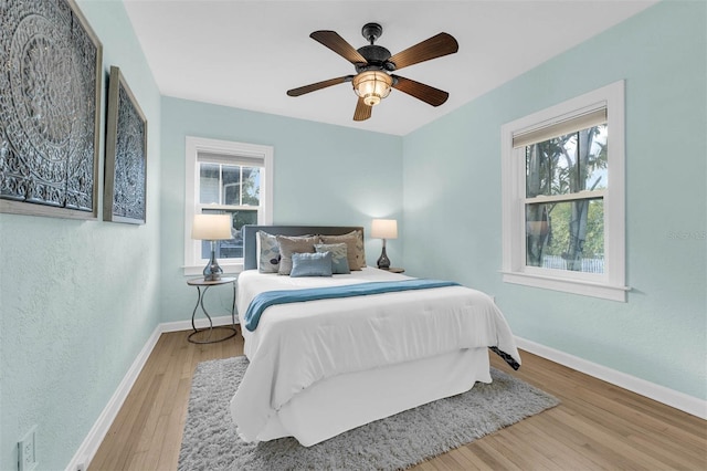 bedroom featuring multiple windows, a ceiling fan, baseboards, and wood finished floors