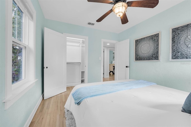 bedroom featuring a ceiling fan, baseboards, visible vents, light wood finished floors, and a spacious closet