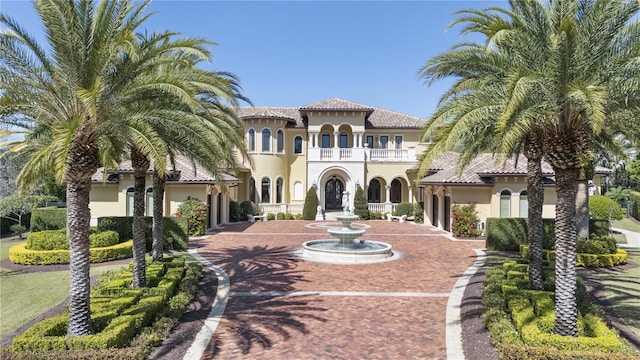 mediterranean / spanish-style home featuring stucco siding, a tiled roof, decorative driveway, and a balcony