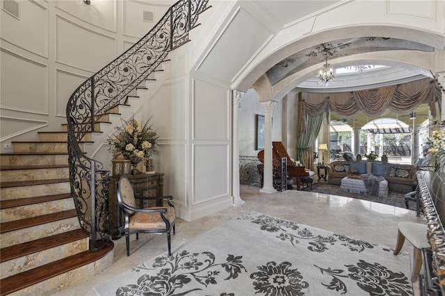 foyer entrance featuring visible vents, ornate columns, arched walkways, a decorative wall, and a chandelier