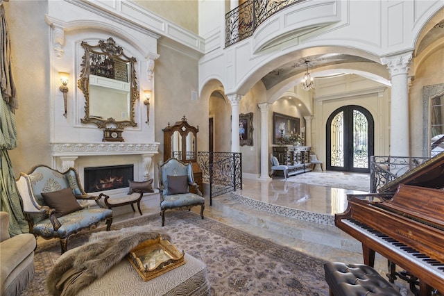 entrance foyer with arched walkways, french doors, a lit fireplace, and ornate columns