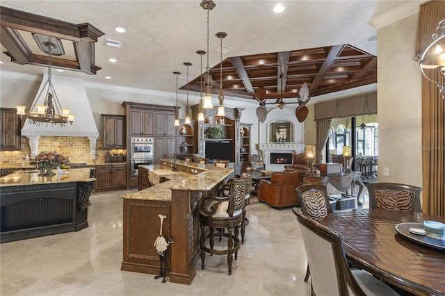 kitchen with visible vents, coffered ceiling, stainless steel double oven, a spacious island, and a lit fireplace