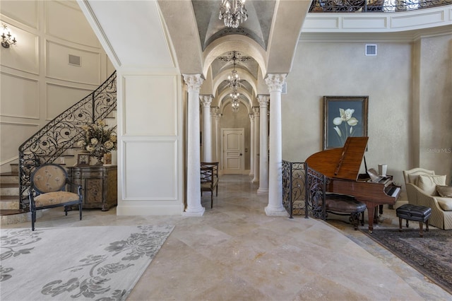 corridor featuring ornate columns, arched walkways, an inviting chandelier, and a decorative wall