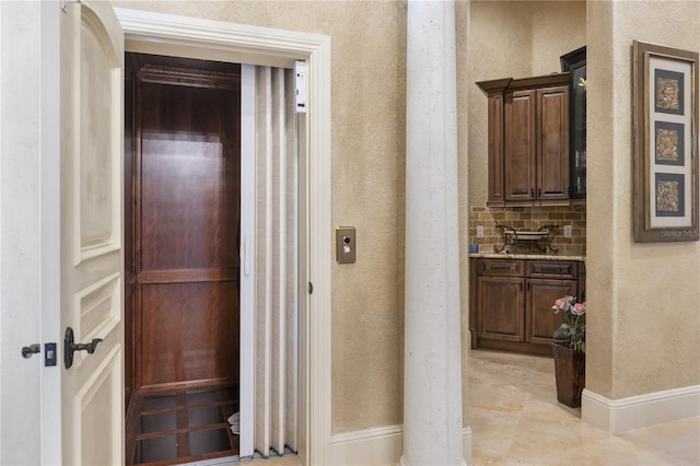 corridor featuring elevator, a textured wall, and baseboards