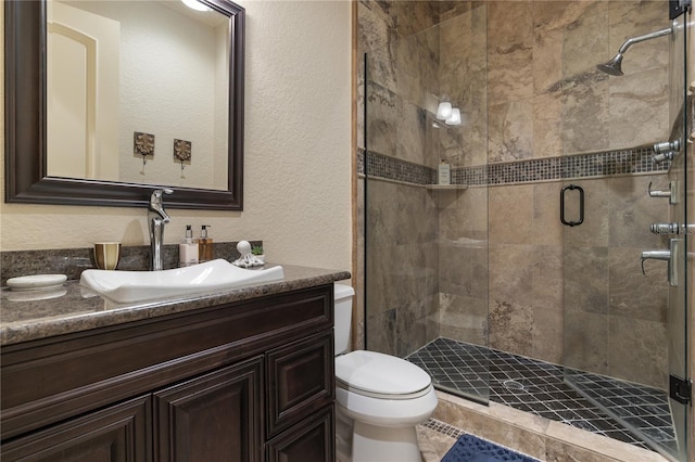 bathroom with vanity, toilet, a shower stall, and a textured wall