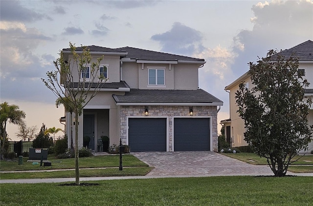 view of front of home featuring stucco siding, decorative driveway, stone siding, an attached garage, and a front yard