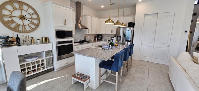 kitchen with light tile patterned floors, decorative backsplash, appliances with stainless steel finishes, white cabinetry, and wall chimney range hood