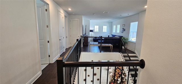 hall featuring wood finished floors, baseboards, a textured wall, visible vents, and an upstairs landing