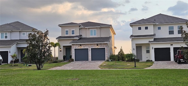 view of front facade with a lawn, stucco siding, decorative driveway, stone siding, and an attached garage