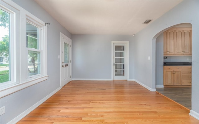 interior space featuring light wood-style flooring, visible vents, arched walkways, and a healthy amount of sunlight