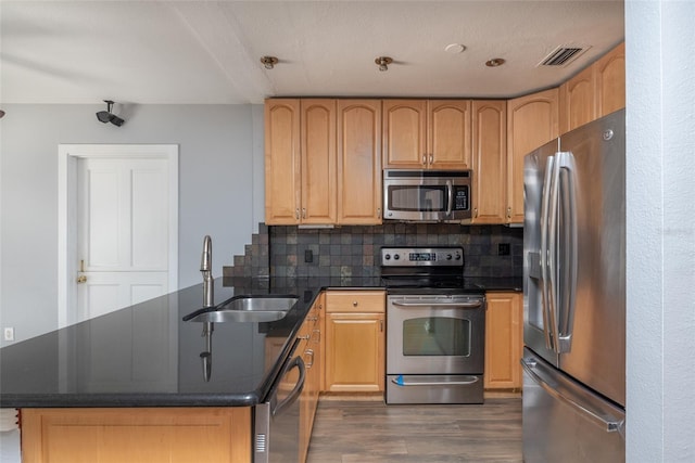 kitchen featuring visible vents, a peninsula, wood finished floors, stainless steel appliances, and a sink