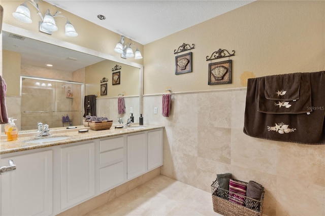 full bathroom with a shower stall, tile walls, double vanity, and a sink