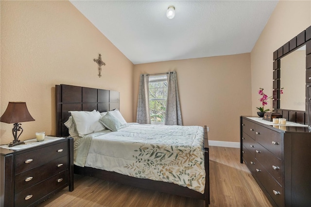 bedroom featuring light wood-type flooring, lofted ceiling, and baseboards