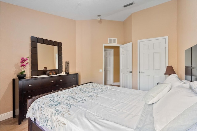 bedroom featuring light wood-type flooring, visible vents, lofted ceiling, and baseboards