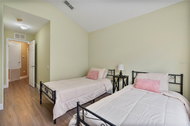 bedroom featuring vaulted ceiling, visible vents, baseboards, and wood finished floors