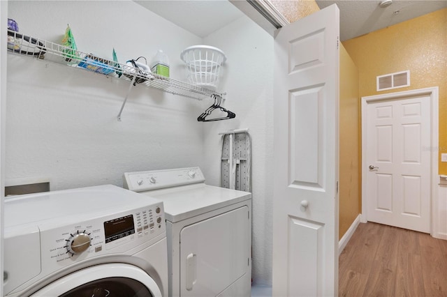 clothes washing area with washing machine and clothes dryer, visible vents, light wood finished floors, baseboards, and laundry area