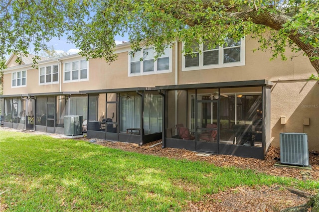 rear view of property with stucco siding, central air condition unit, a yard, and a sunroom