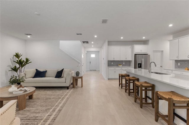 kitchen with a breakfast bar area, stainless steel fridge with ice dispenser, a sink, light countertops, and white cabinets