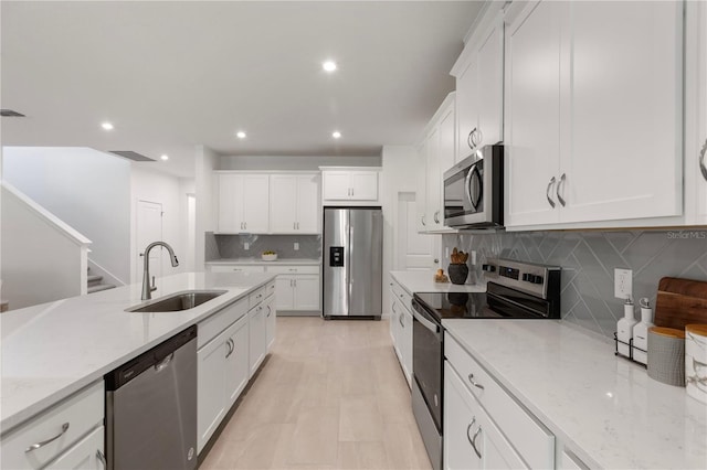 kitchen with a sink, light stone counters, tasteful backsplash, stainless steel appliances, and white cabinets