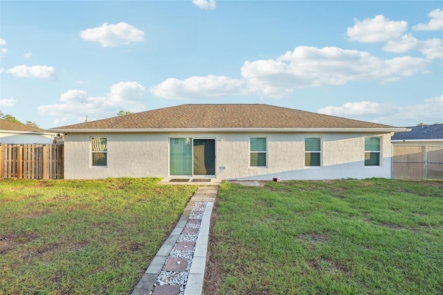 rear view of house with a lawn, fence, and stucco siding