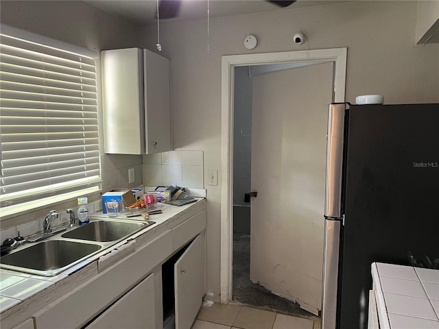 4845 Elese St, Orlando, FL 32811 - kitchen with tile counters, a sink, freestanding refrigerator, white cabinetry, and light tile patterned floors
