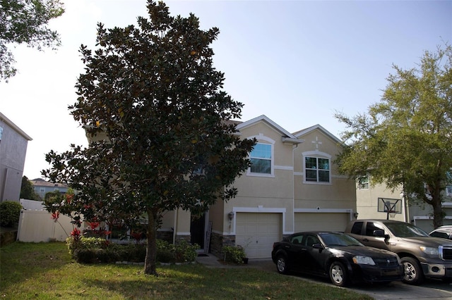 view of front of home featuring stucco siding, stone siding, fence, a front yard, and a garage