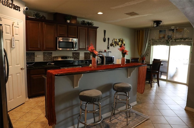 kitchen featuring a kitchen bar, dark countertops, light tile patterned flooring, and appliances with stainless steel finishes