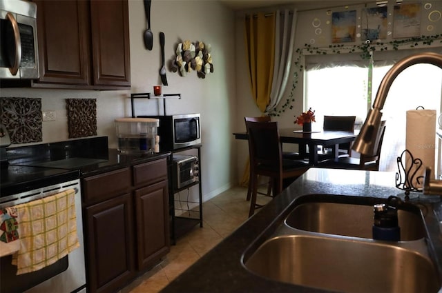 kitchen with baseboards, dark brown cabinetry, light tile patterned flooring, stainless steel appliances, and a sink