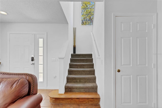 tiled entrance foyer featuring baseboards, a textured ceiling, and stairs